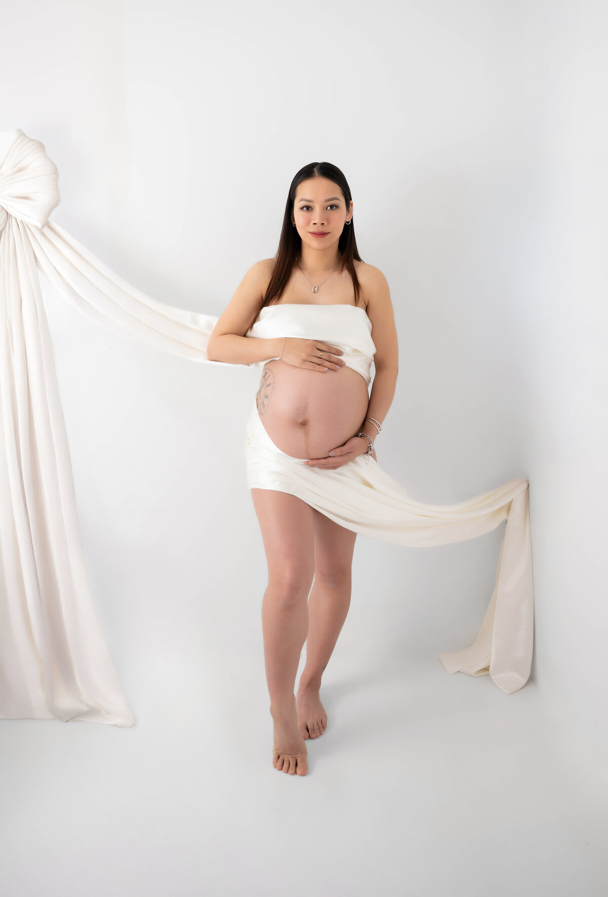 Expectant mother showcasing her bump, wrapped in an off white silky fabric for her maternity pictures in Chicago, IL.