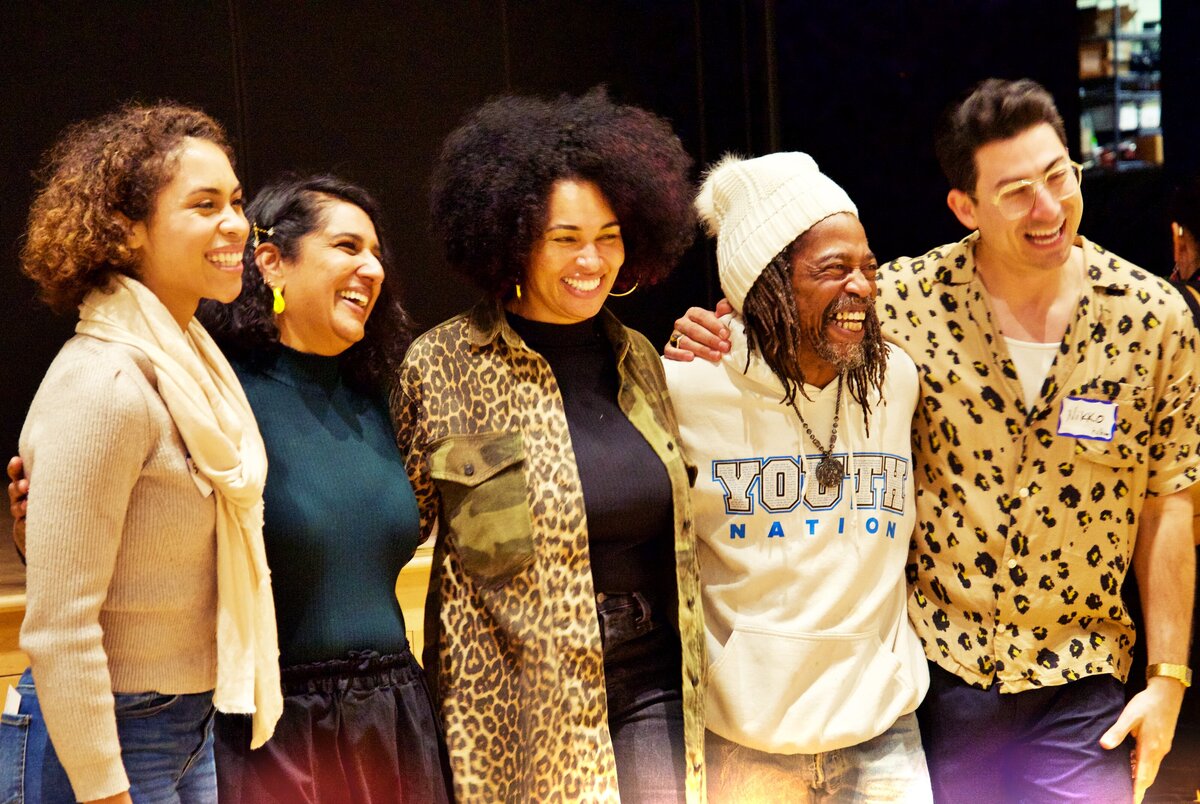 Five people smiling in a line posing for the photo arms linked around shoulders