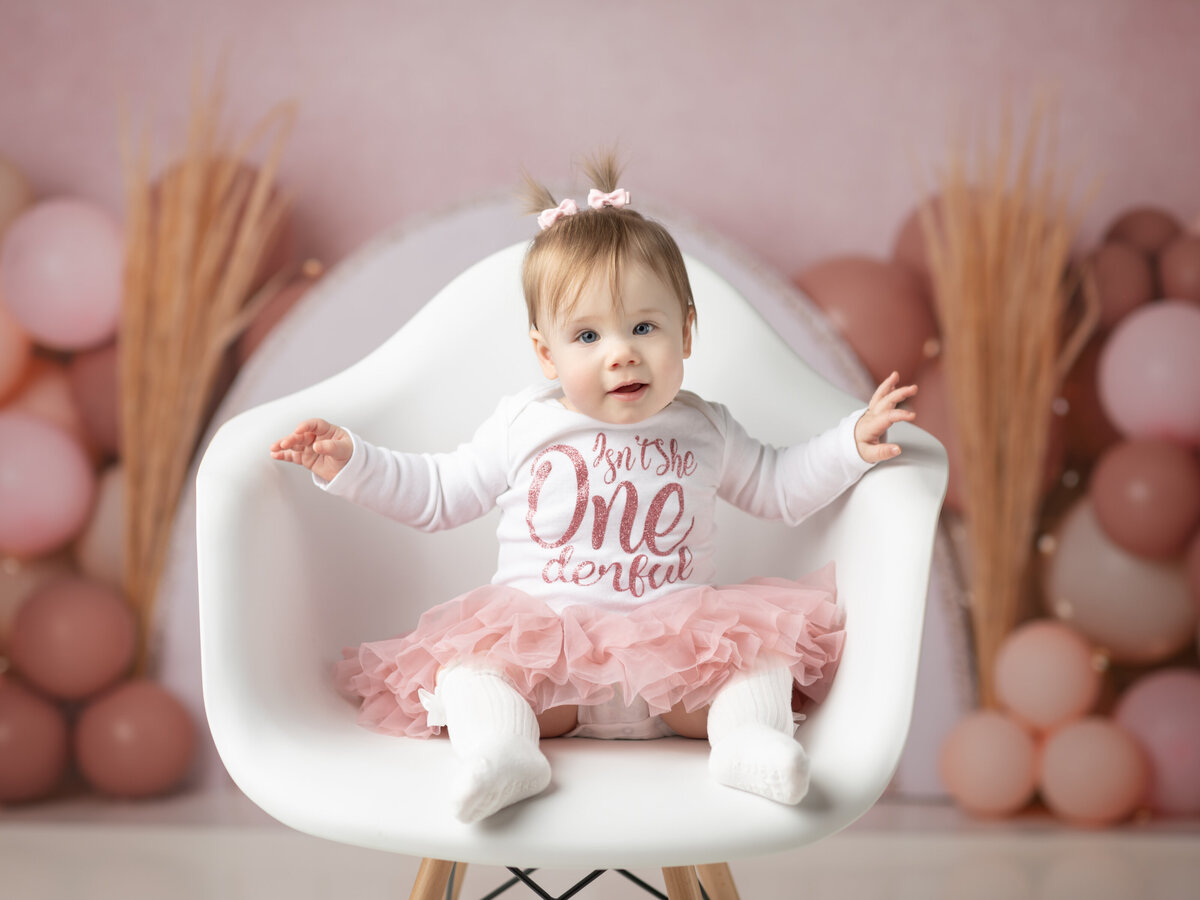 one year old girl sitting in white chair for cake smash photoshoot