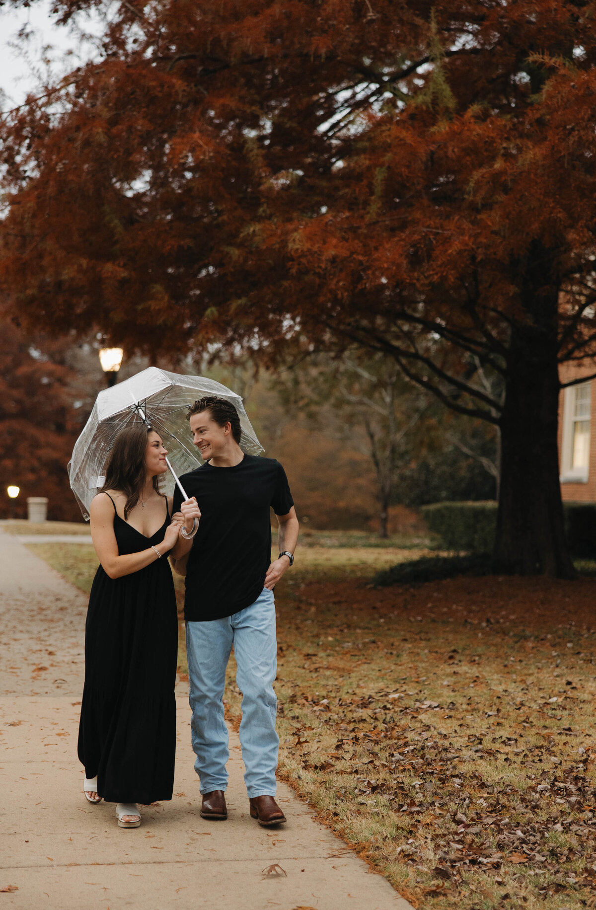 engaged couple walking across campus at Samford university in the rain with a Clear umbrella