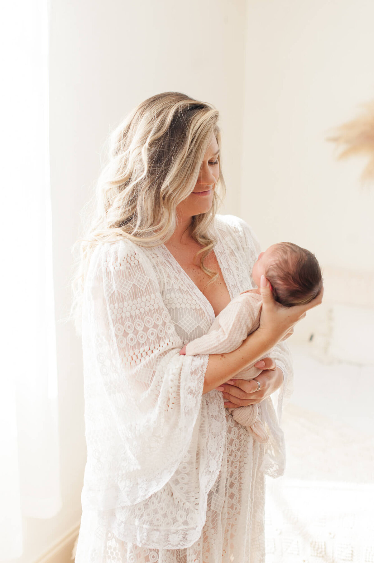 Mom holding newborn baby while standing near a natural light window