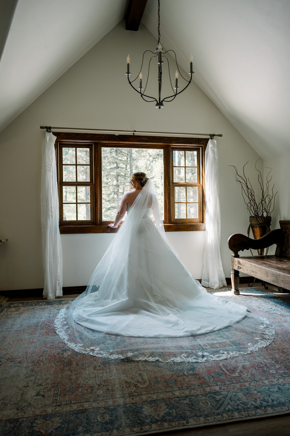 Bride in a flowing wedding gown standing by a window, showcasing her silhouette during her Montana summer wedding.