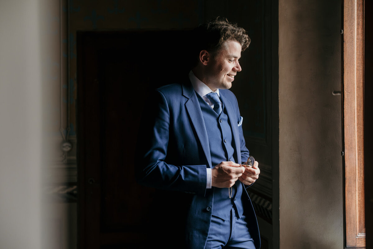Portrait of groom ready for his big day, looking out of a window, holding a pocket watch.