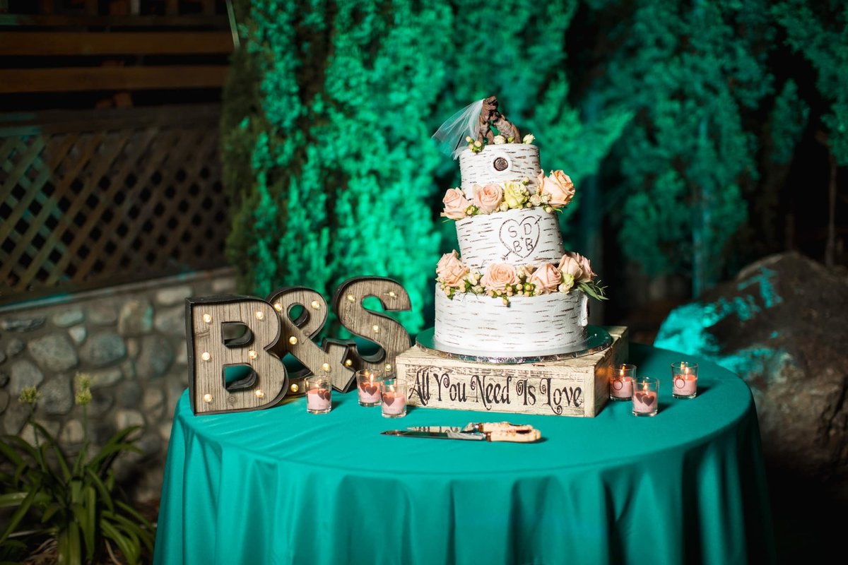 Night shot of the 3-tiered white wedding cake sitting on a table with a teal tablecloth and the couple's initials