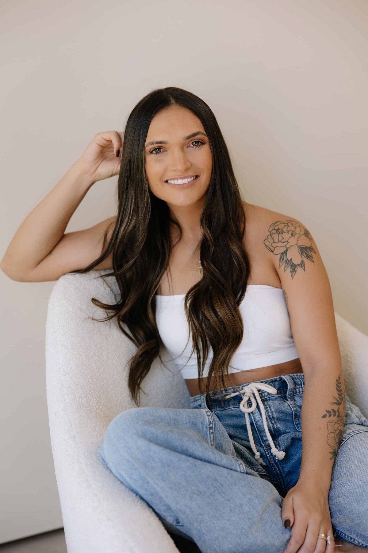 A woman poses for a photo while sitting on a white chair. 