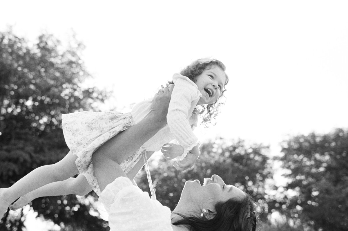 candid family photo of toddler girl being swung around by her mother while she smiles 