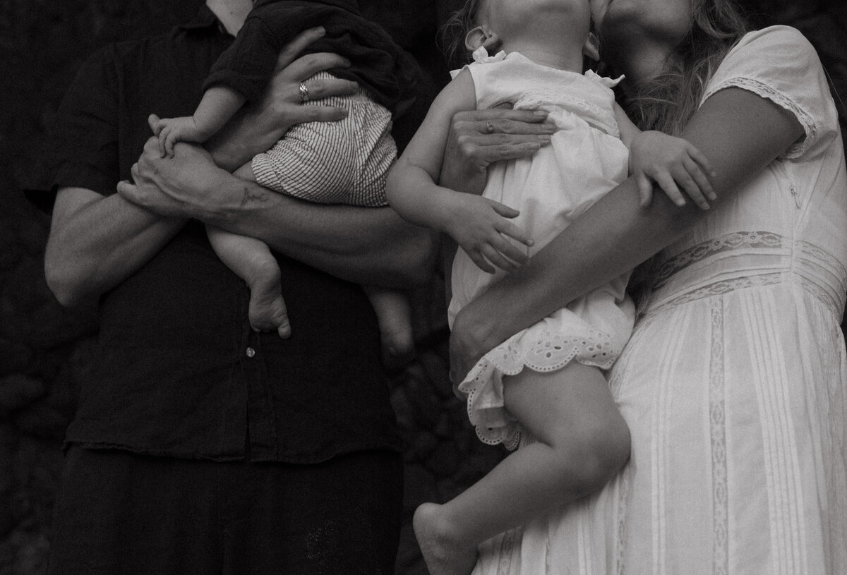 A family of four hugging and cuddling closely with baby and toddler legs in the frame
