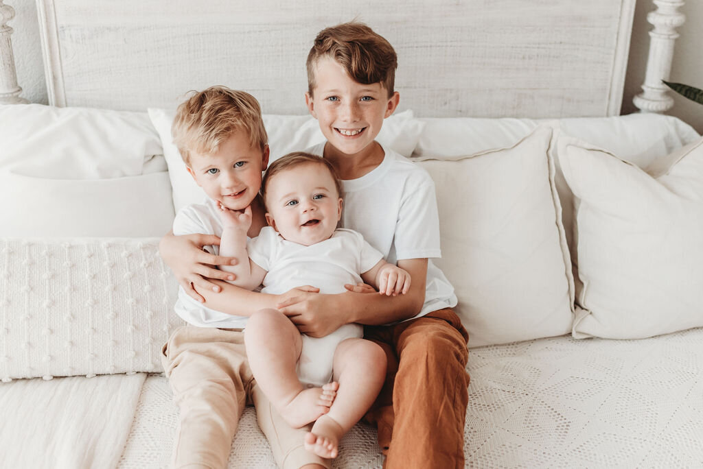 three boys sitting on day bed hugging