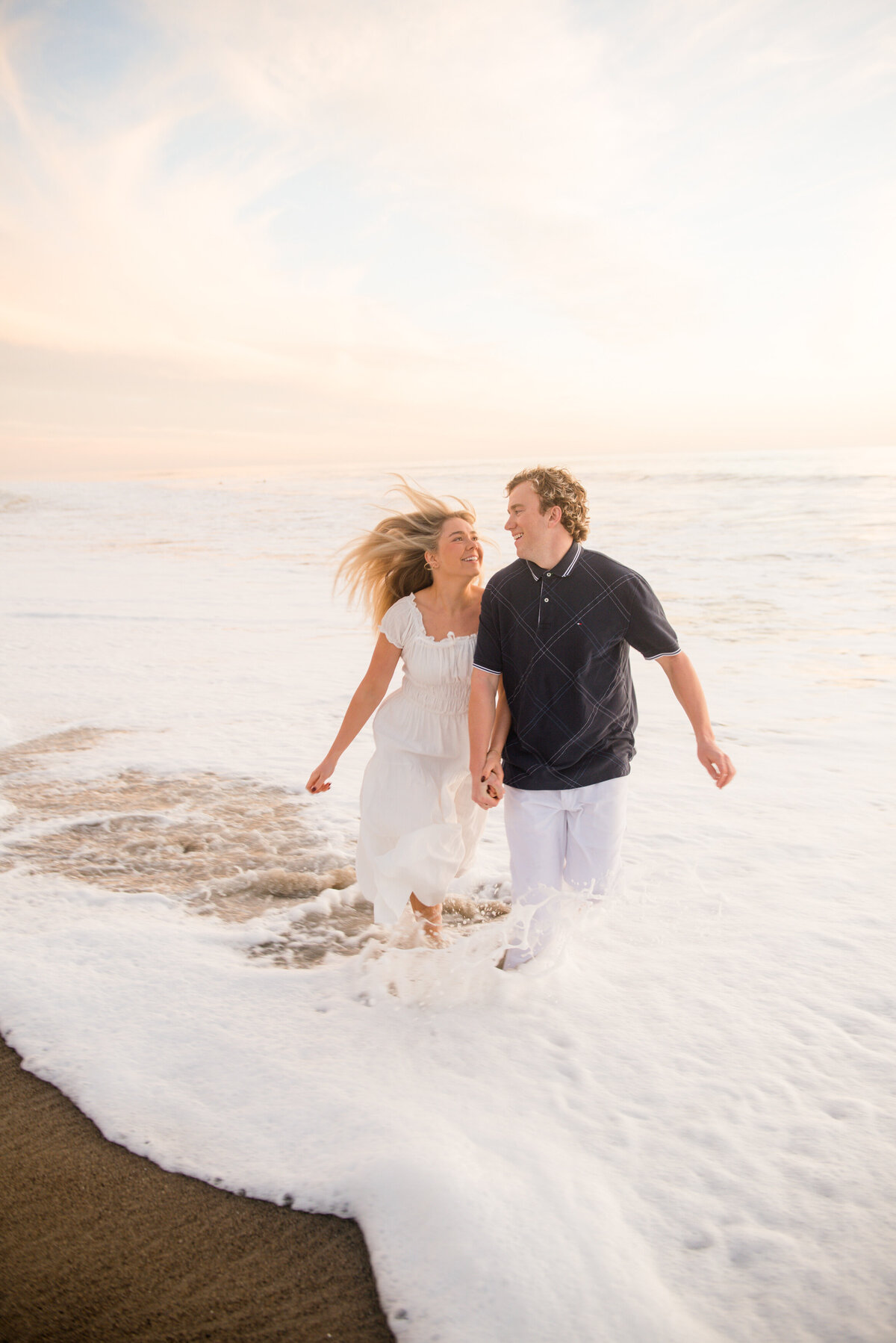 adventurous couple running in the waves during couples session by wedding photographer mattie taylor in san diego