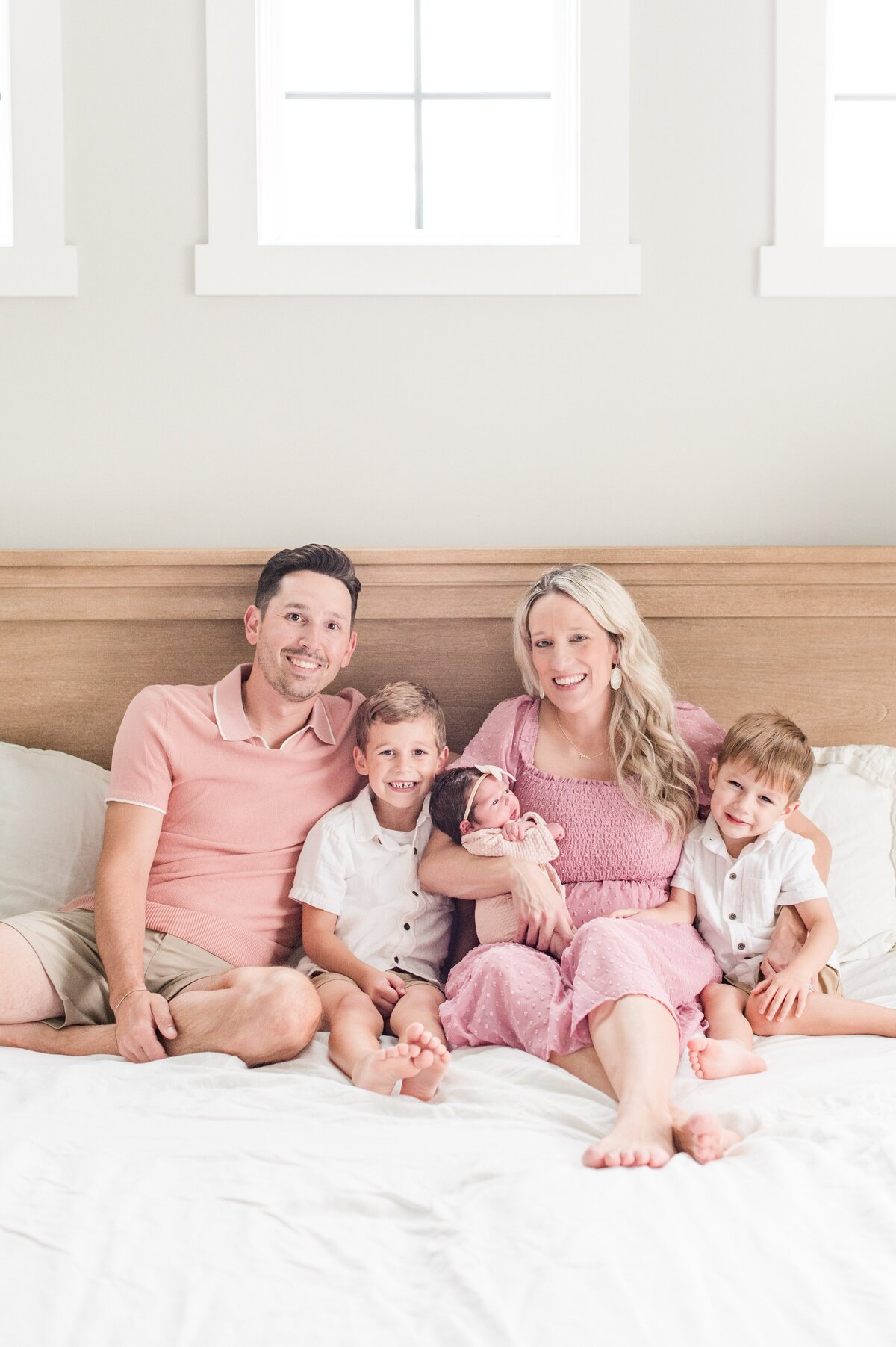 family of five in bed wearinh pink hues with newborn