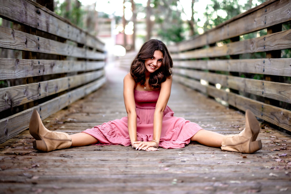 High school senior girl posing cheeky with legs spread and hands placed directly in front of her on rustic wood pier at the lake in Orlando
