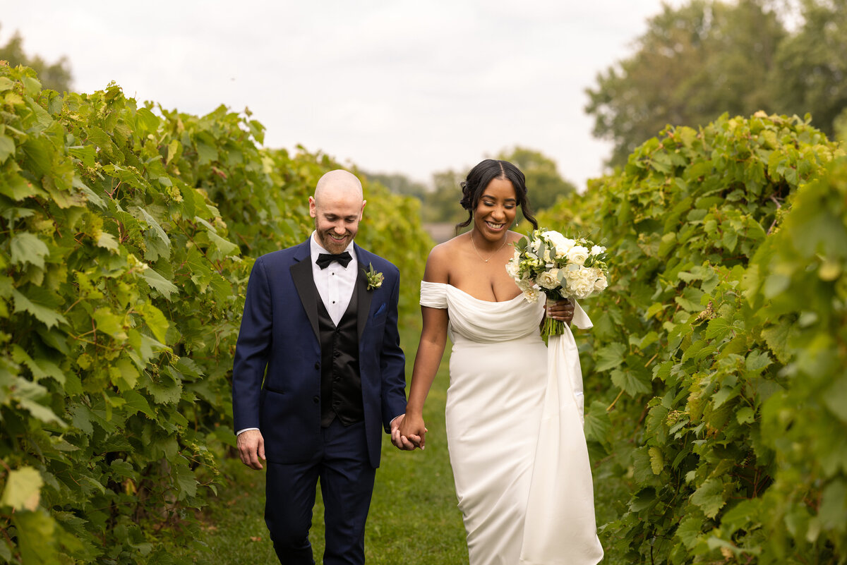 Groom and bride happily walk down the aisles of a vineyard in Ohio. Photographed by Aaron Aldhizer