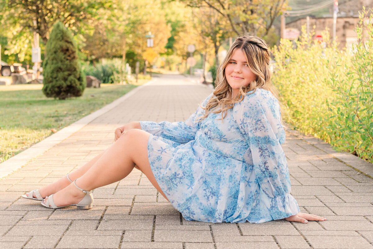 High school senior sitting on a brick path in a blue floral dress — Class of 2025 photos by Bree Stewart of Lens Love Photography in Ohiopyle, PA.