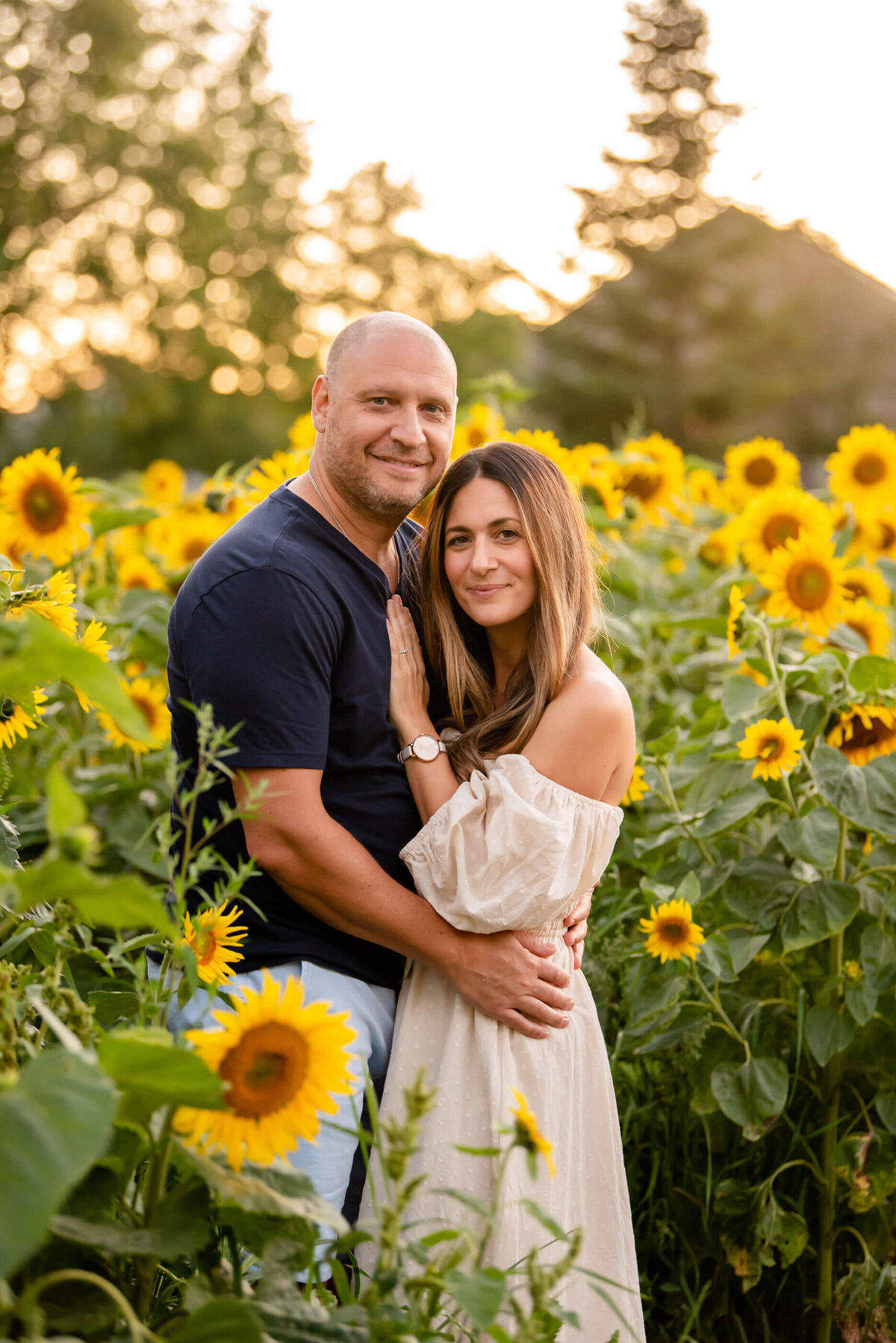 husband and wife hugging in a sunflower field for their summer family photos in Burlington, On