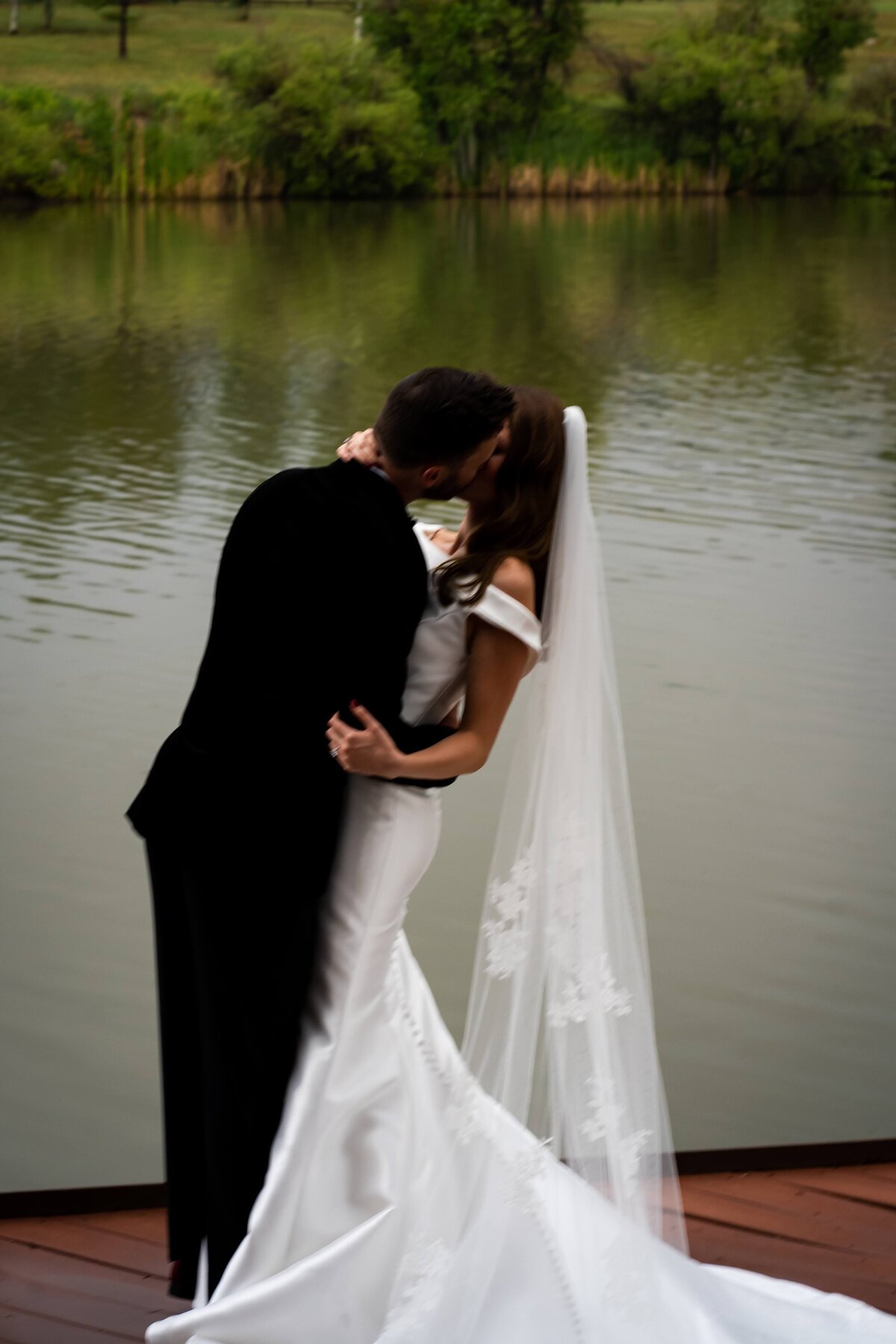 Bride and groom share a kiss in front of the pond at Spruce Mountain Ranch.