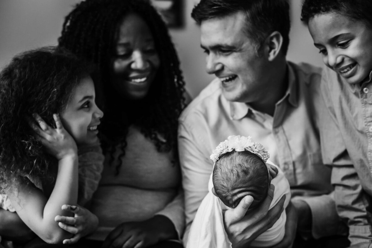 smiling family on couch holding new baby and looking at eachother