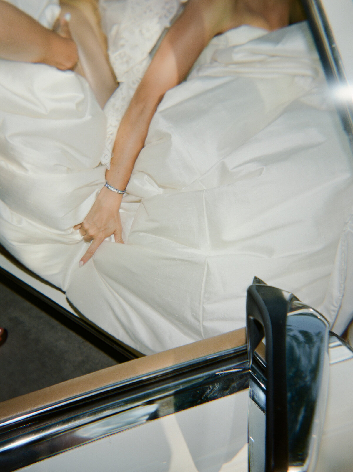 editorial, unique film wedding photography shows a bride fitting her large silk Leah Dagloria ballgown into a vintage car on her wedding day
