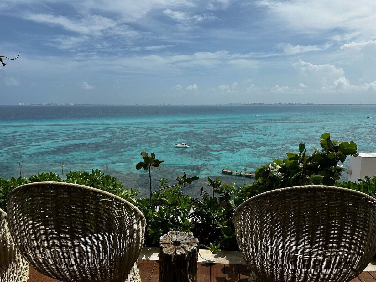 Two chairs overlooking an expansive view of the ocean with clear blue waters, a peaceful and scenic spot at a seaside destination.