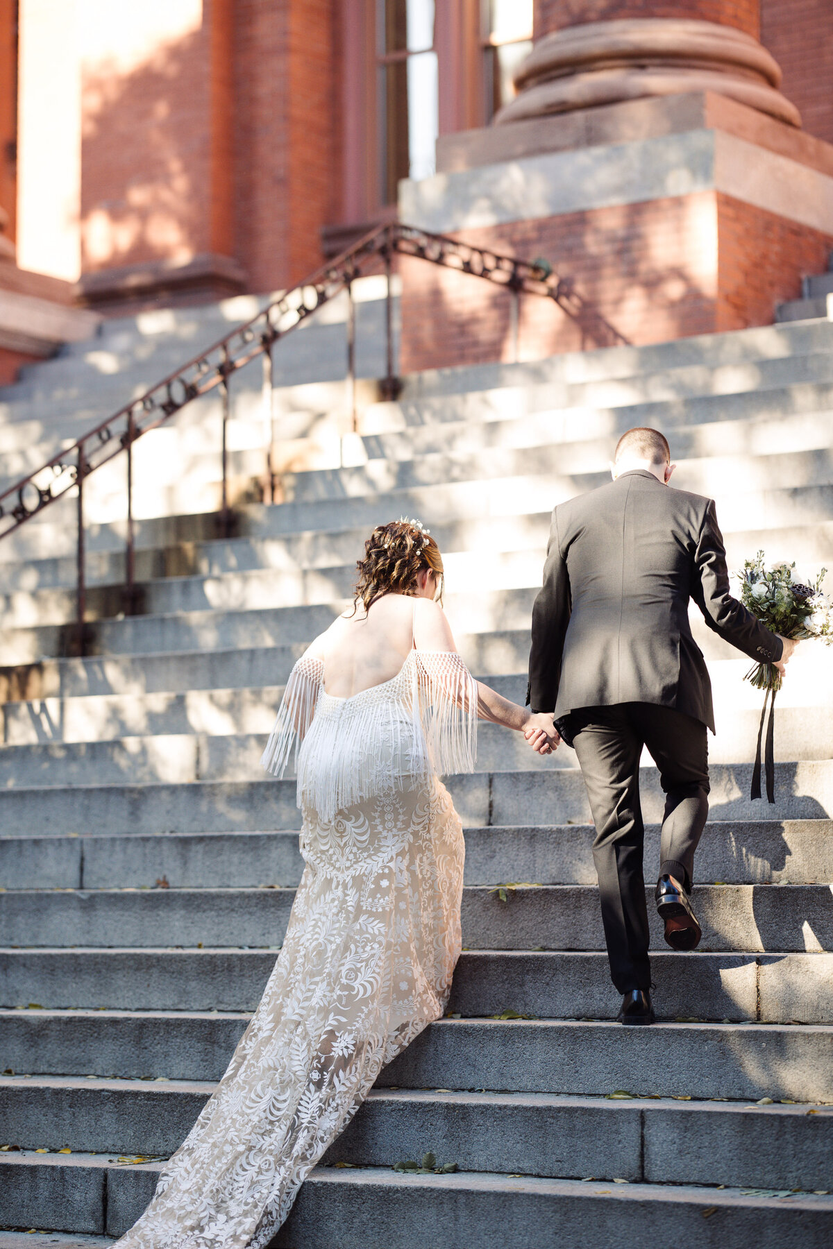 Bride and groom walk up steps of Multicultural arts center in MA with dappled light. Flowers by Haven Floral company.