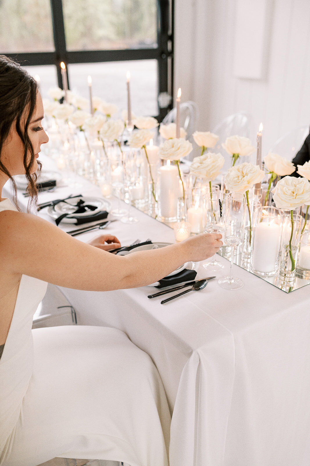 A bride sits at a table and reaches for a glass at a styled wedding photography session.