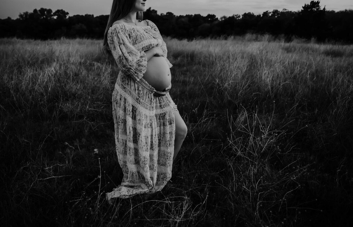 black and white photo of a pregnant woman with her belly exposed. She is standing in a field of glowers and grass and wearing a two piece set