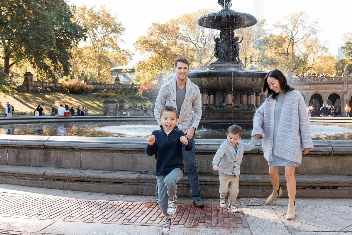 Family Photographer, a young family holds hands together near a park fountain