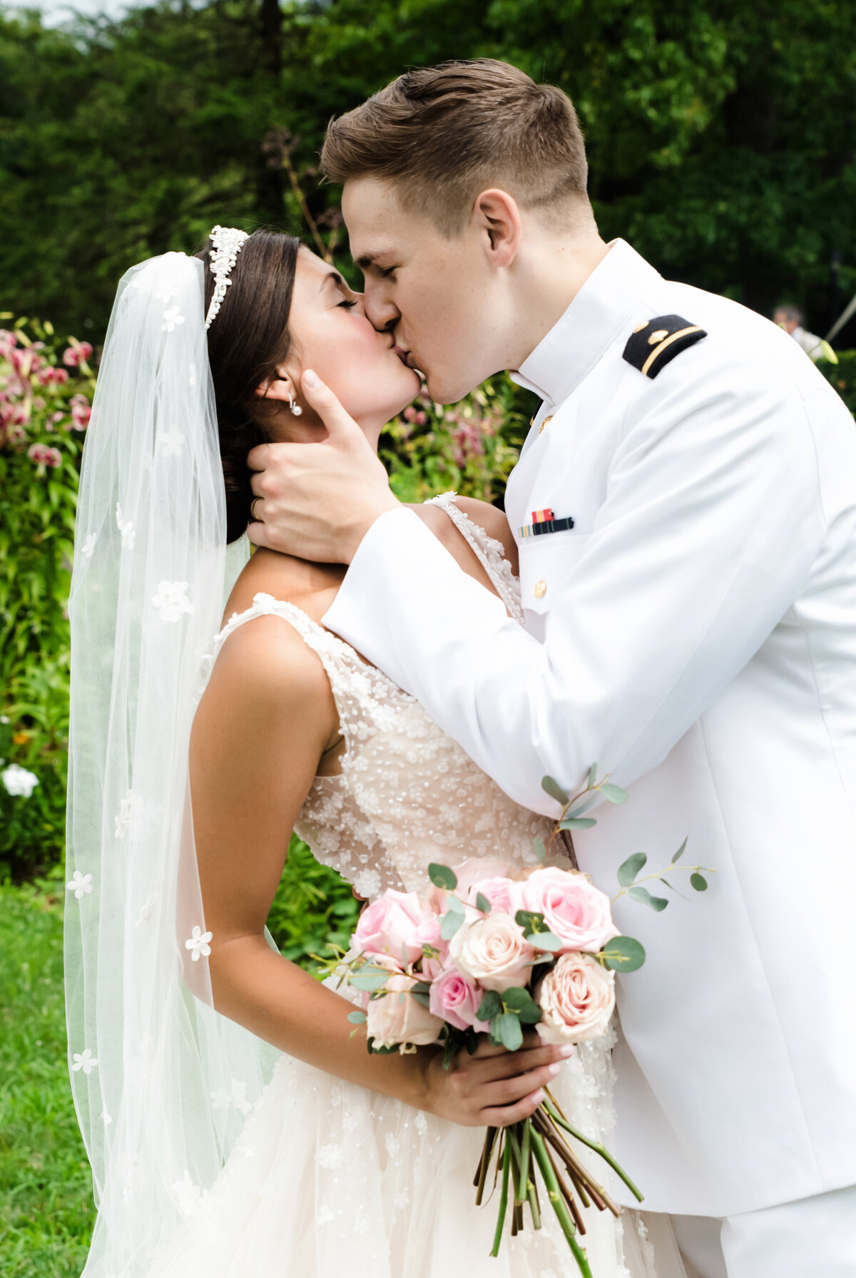 bride and groom kiss in garden while bride holds blush bouqet