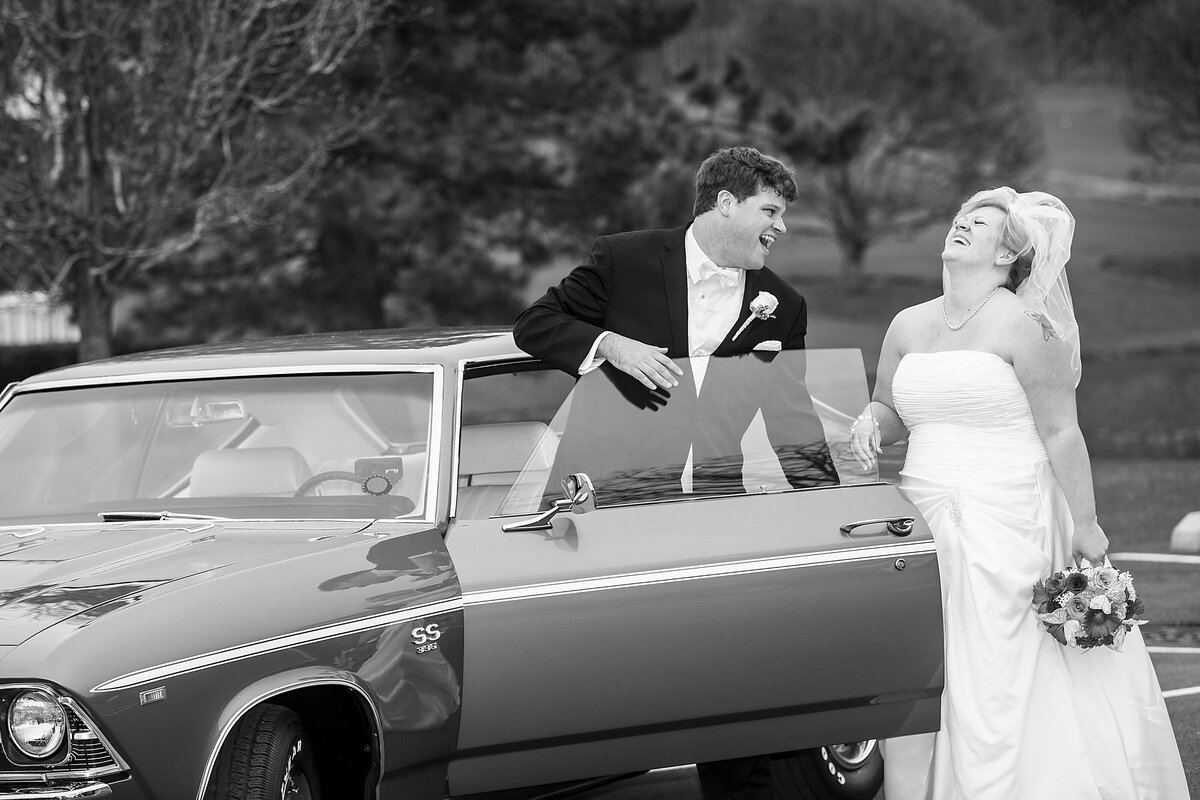 A bride and groom laugh as they get into a vintage car.
