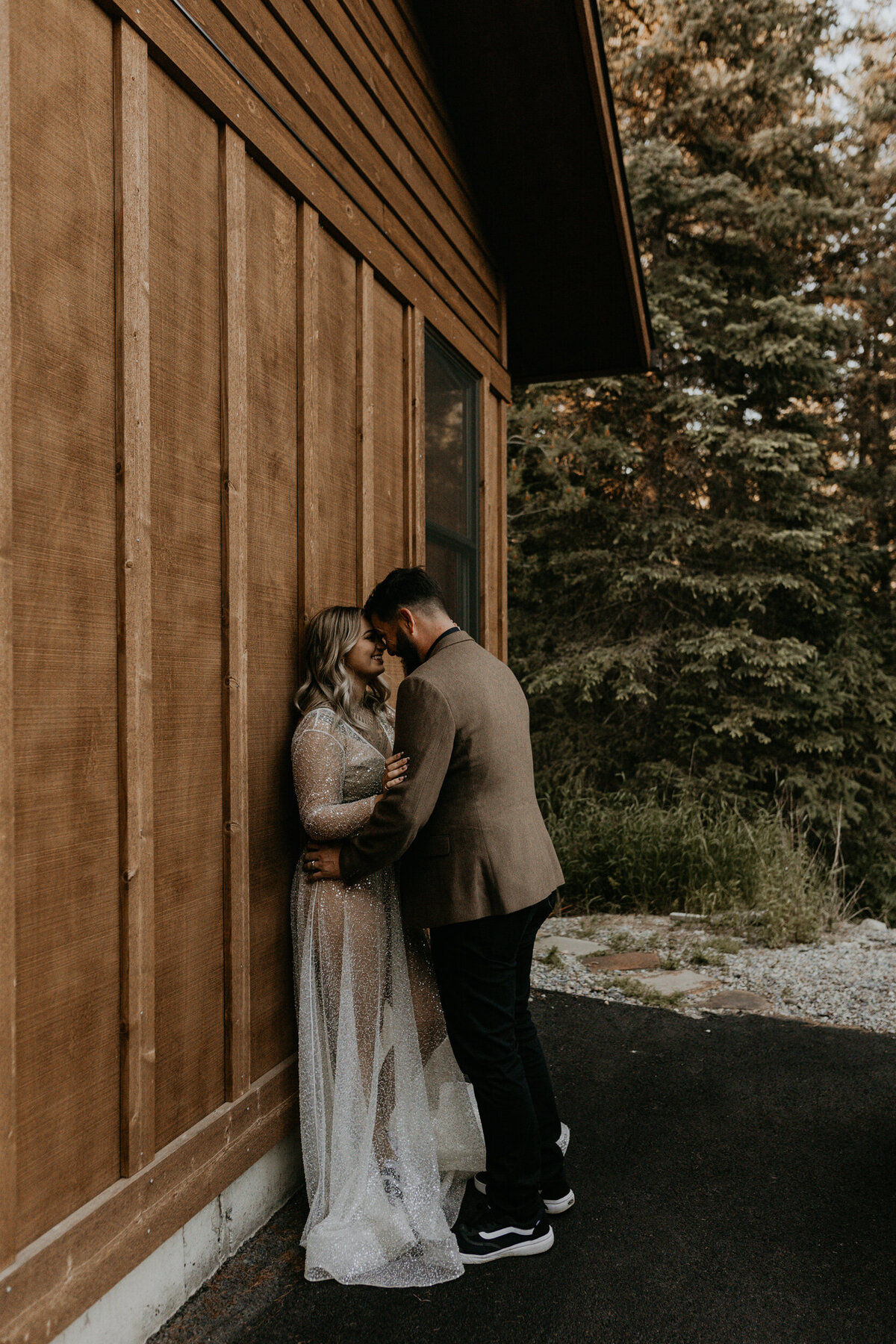 newlyweds standing against a cabin in their wedding attire