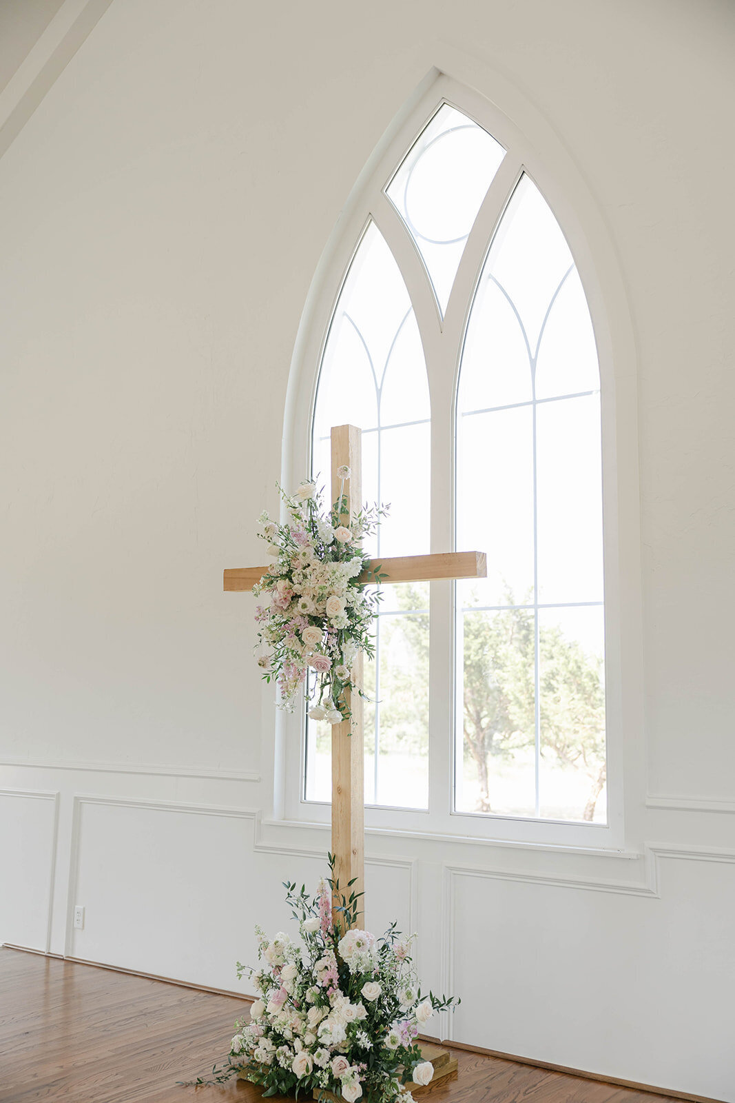 a wooden cross in chapel with soft pick flower arrangement