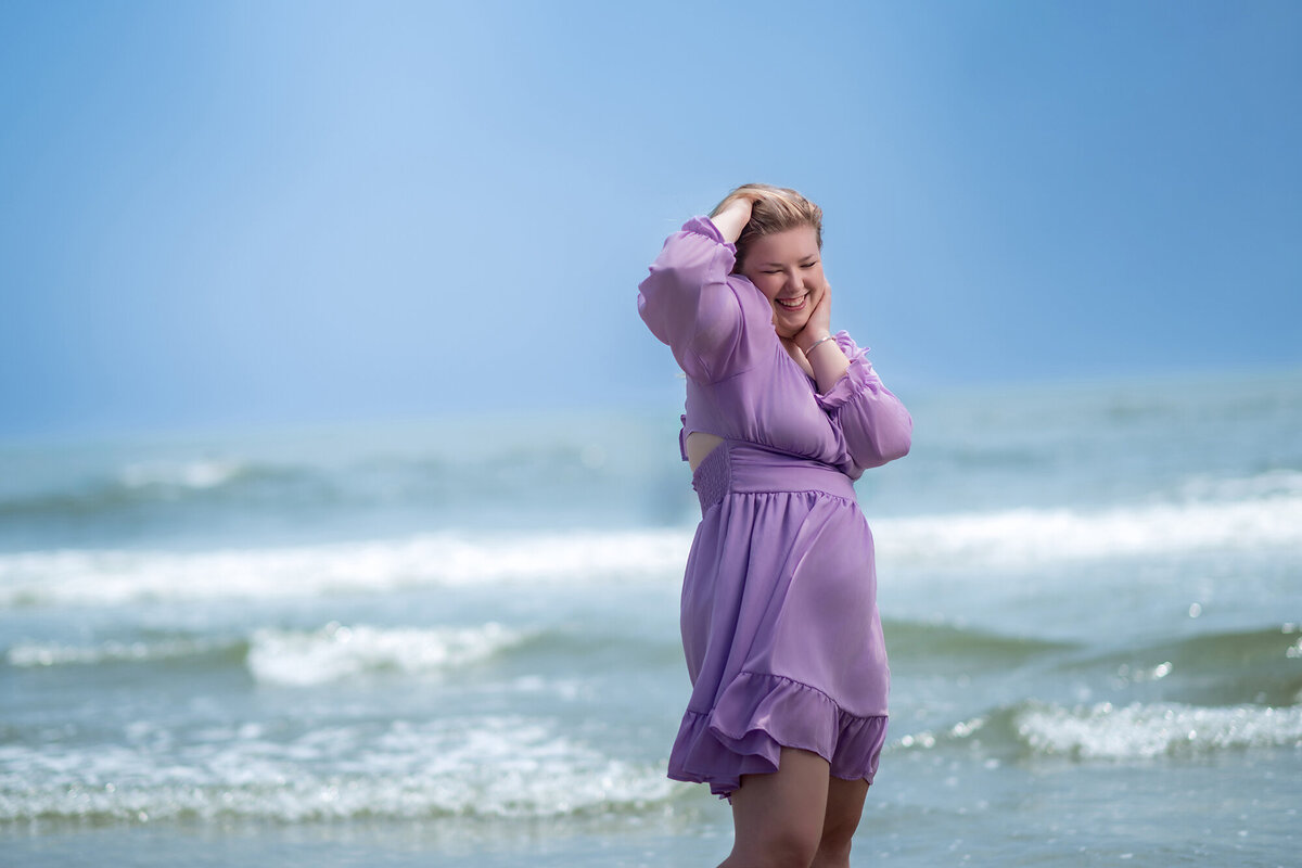 A woman in a purple dress laughs while standing on a beach