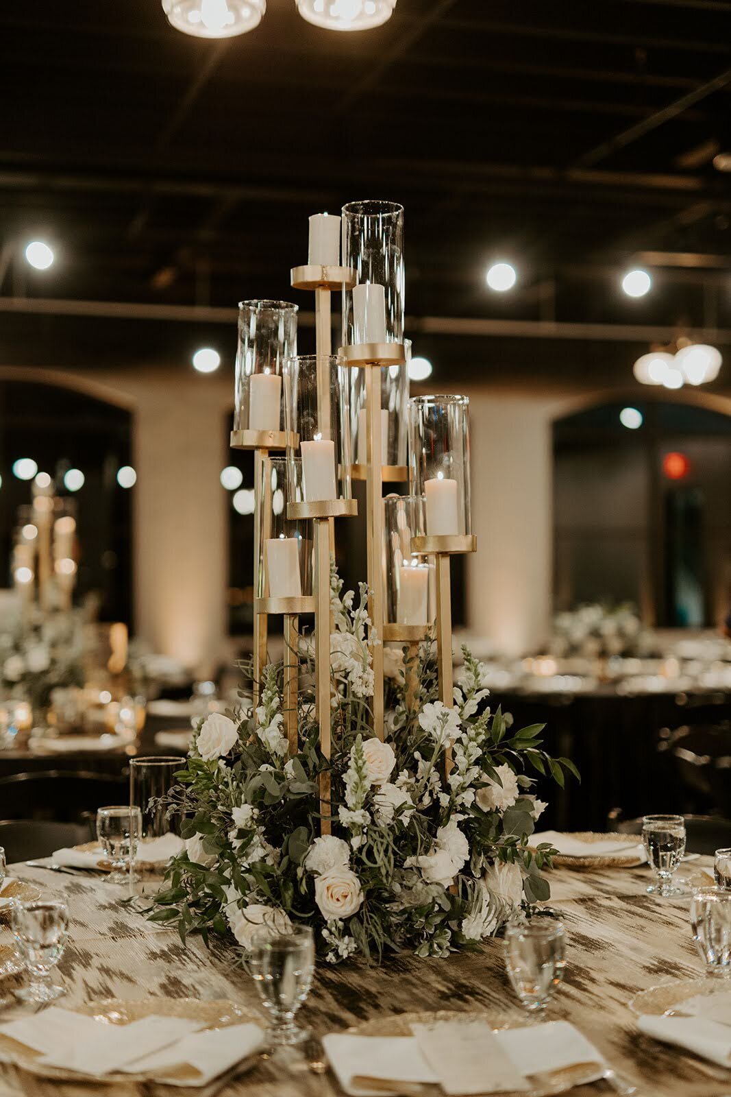 White floral and greenery wedding reception centerpieces filled with gold multi leveled candles at the Bowery House and Gardens.
