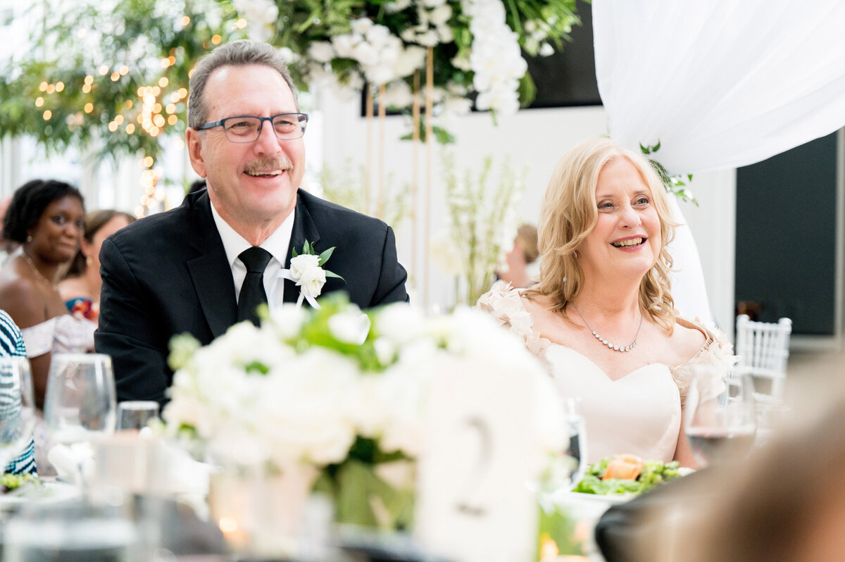 parents of the bride smiling as they listen to a wedding toast