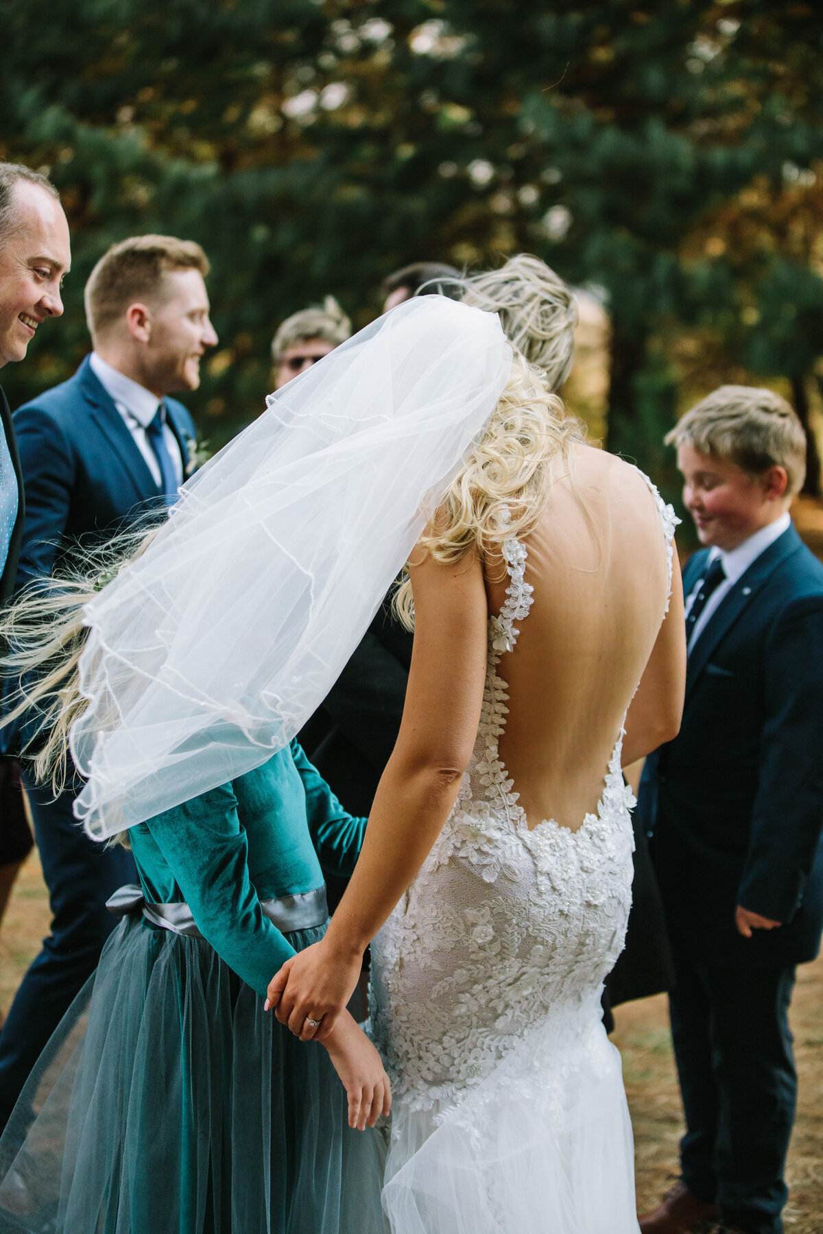 Guests greet the bridal couple as the wind blows the bride's veil in the air. 