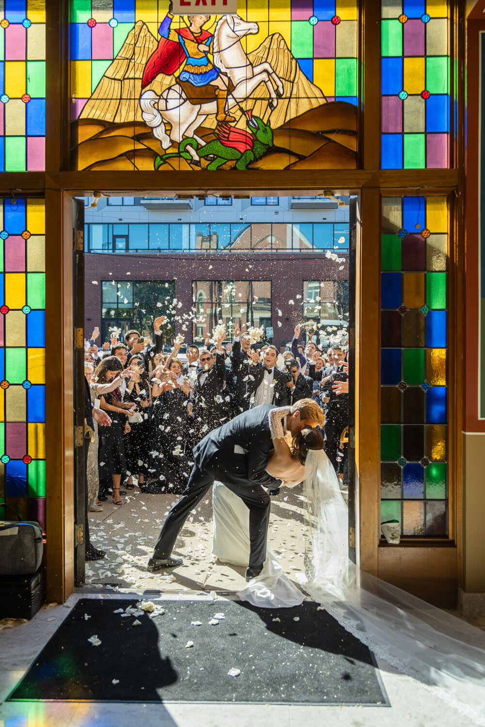 A bride and groom kissing in front of a stained glass window