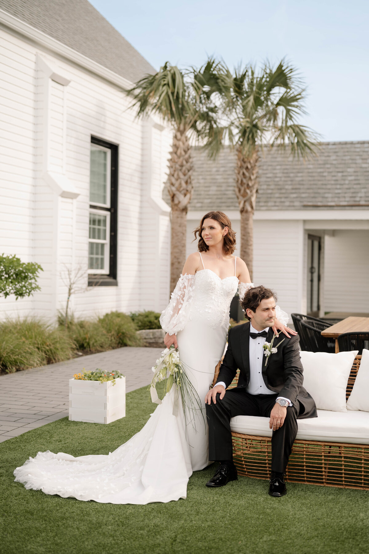 A bride and groom lean over a champagne tower, both sipping from green glassware.