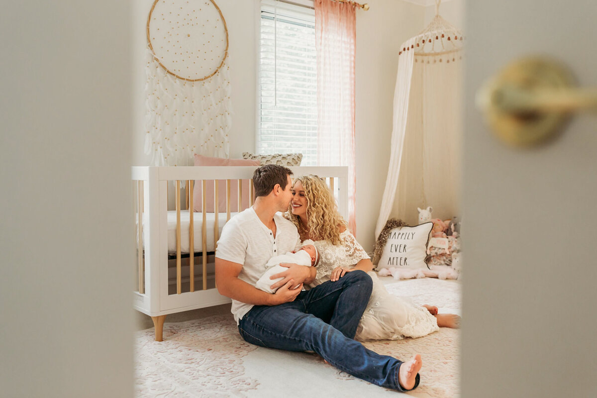 parents kiss holding baby in newborn room
