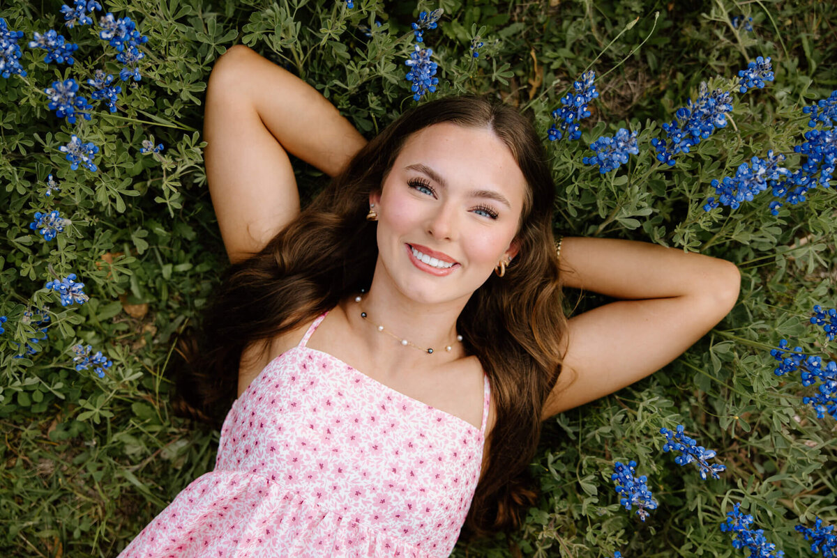 senior girl in pink dress laying in a field of bluebonnets