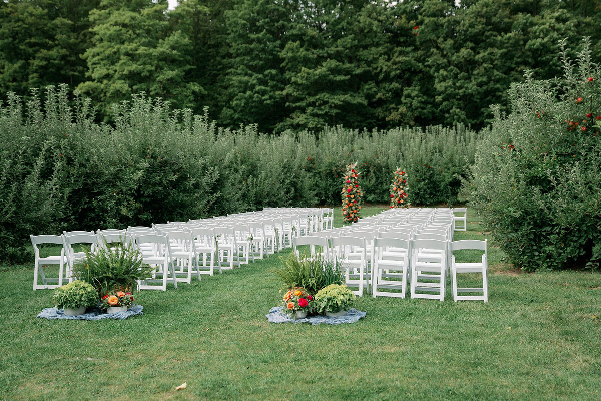 Wide ceremony view featuring the floral arch, orchard trees, and guest seating at a September wedding at The Cherry Barn in Frankfort, Michigan.