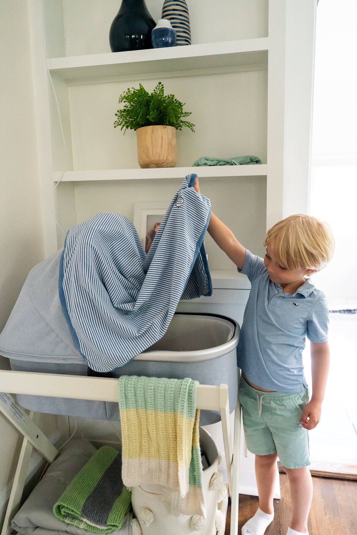 brother lifting blanket off bassinette to show sleeping newborn baby