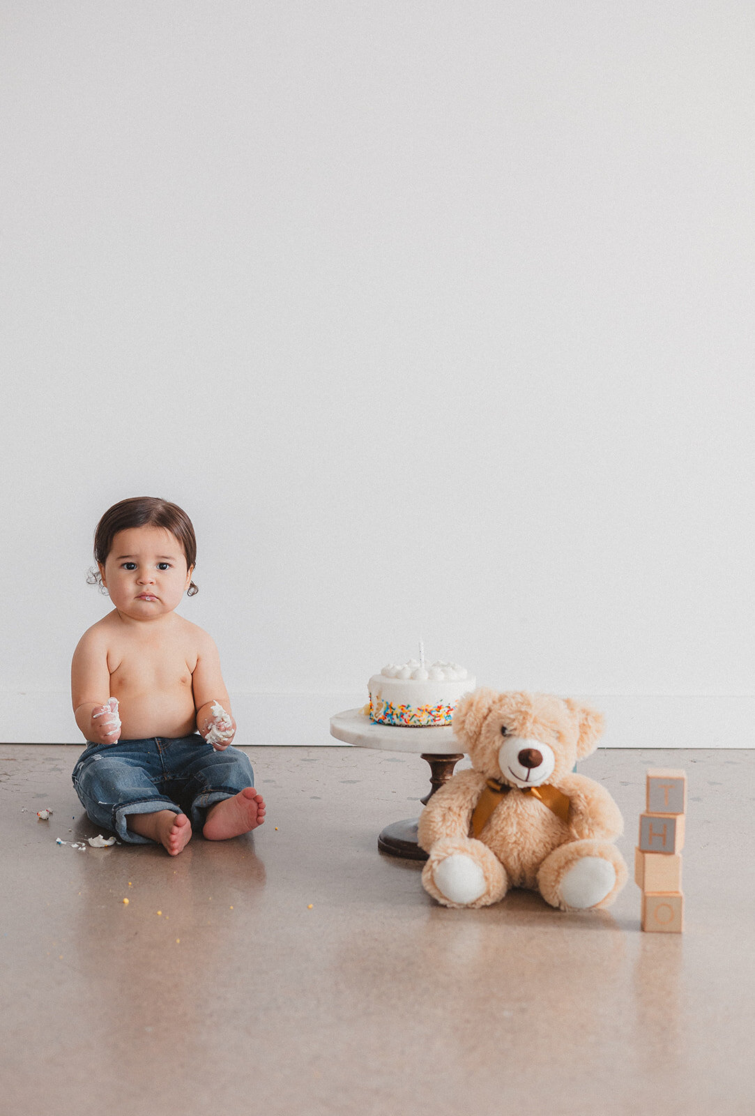 A little boy sits next to cake and a teddy bear.