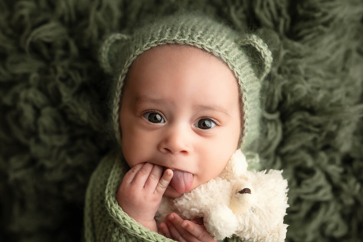 Baby boy stares into the camera wearing a green bear bonnet.