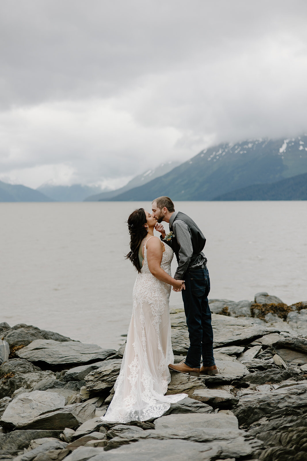 Elopement couple kiss on Alaska rock shoreline.