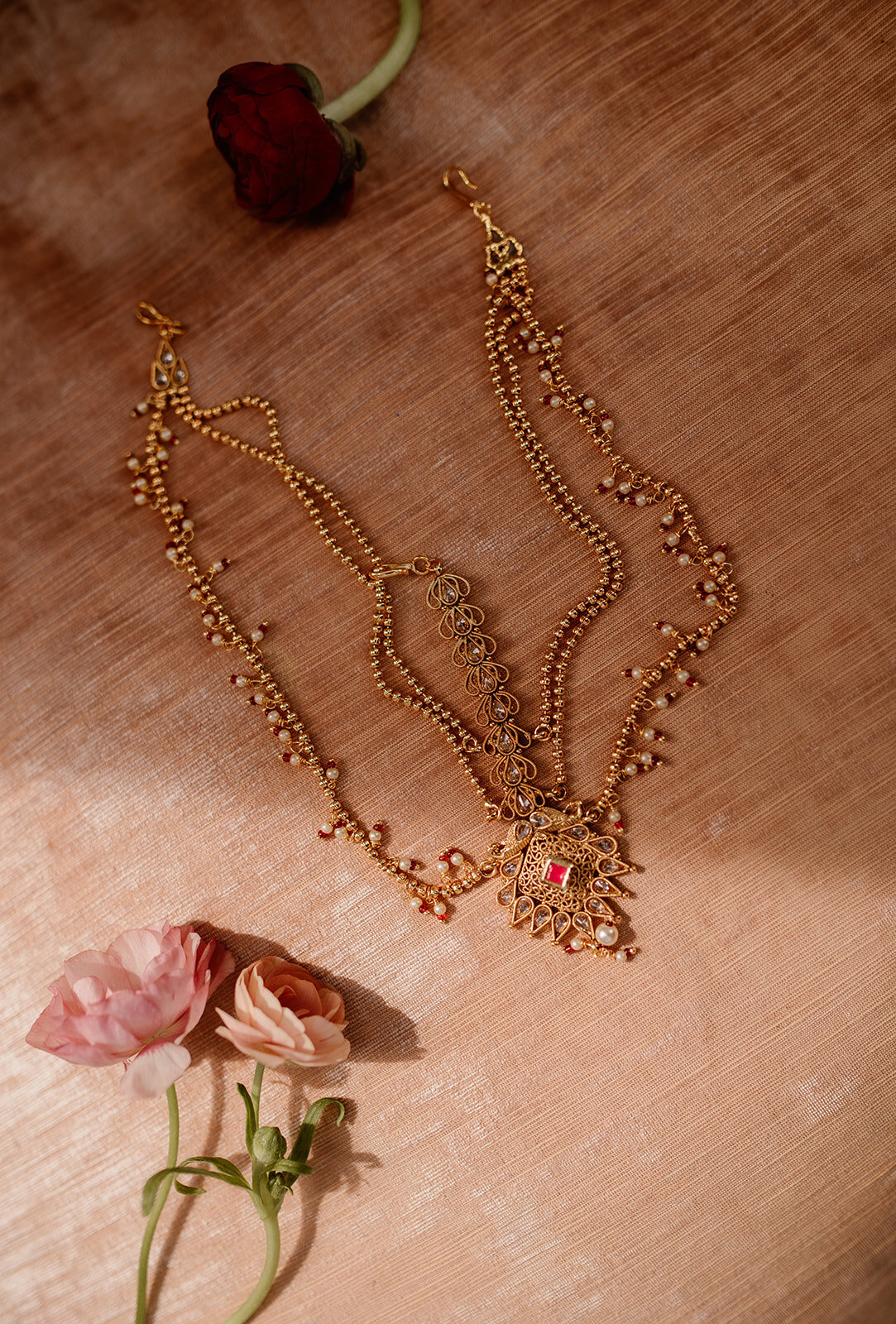 A delicate gold necklace with traditional Indian detailing, placed elegantly on a textured surface with soft floral accents.