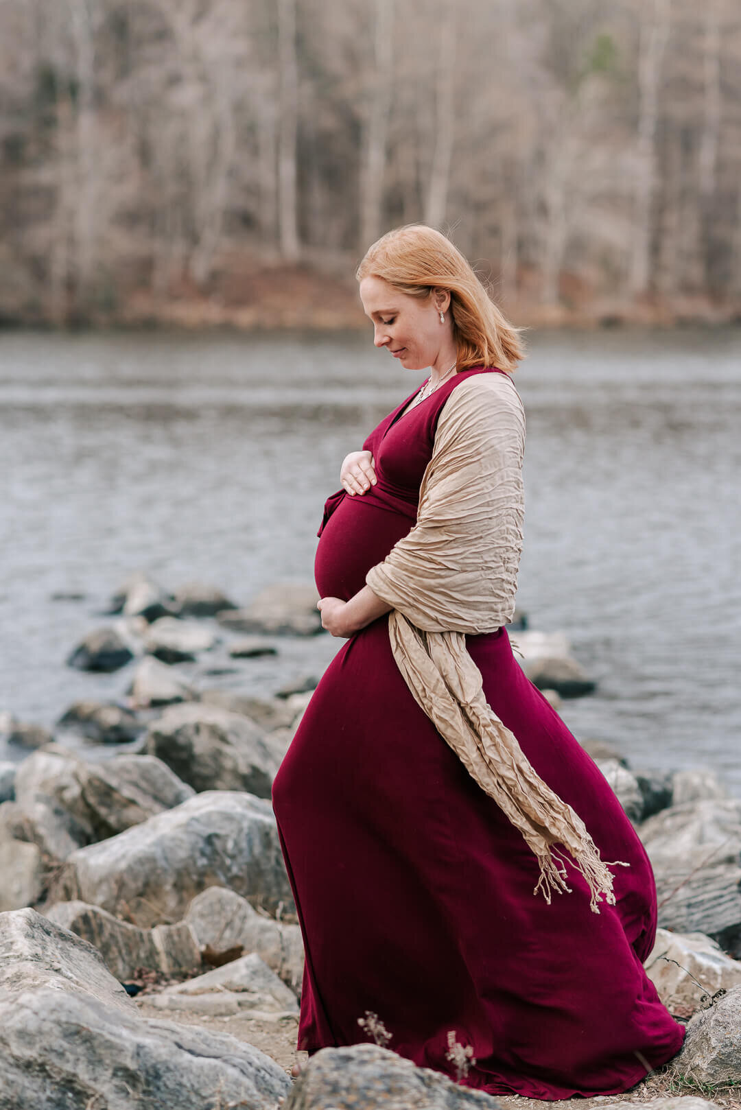 A woman holding her pregnant belly while her burgundy dress billows in the wind