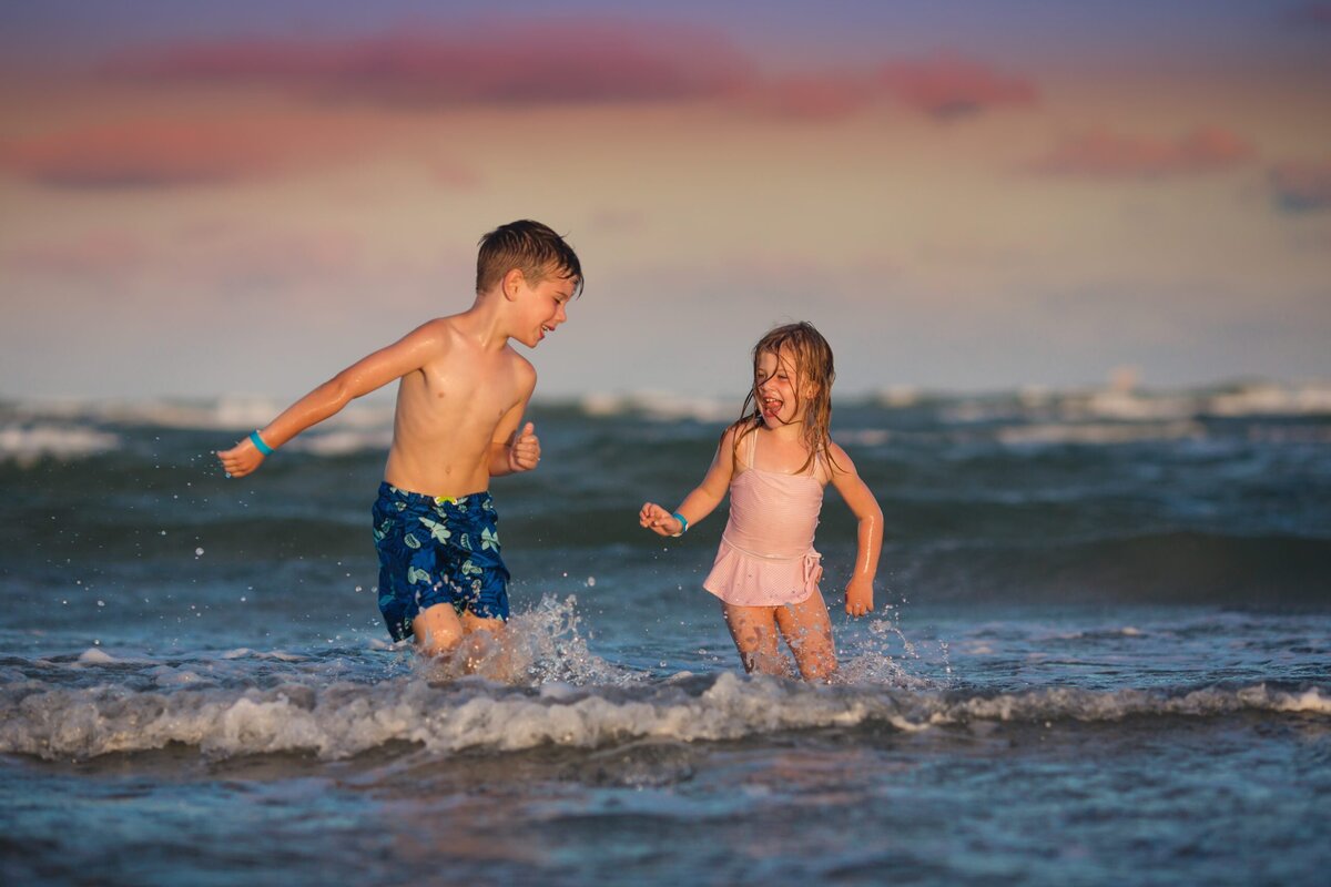 Two children play in the beach at sunset.