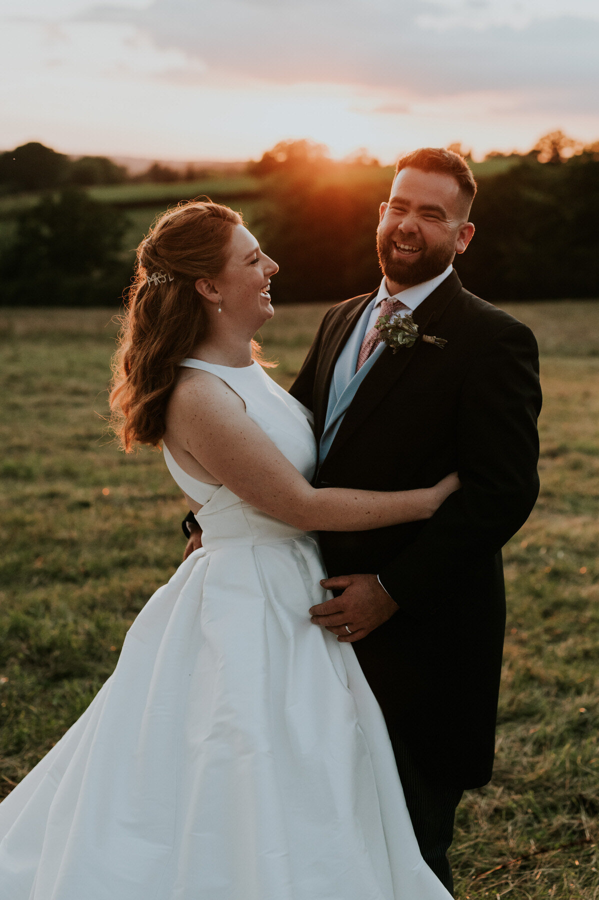 Bride and groom laughing in a field at golden hour