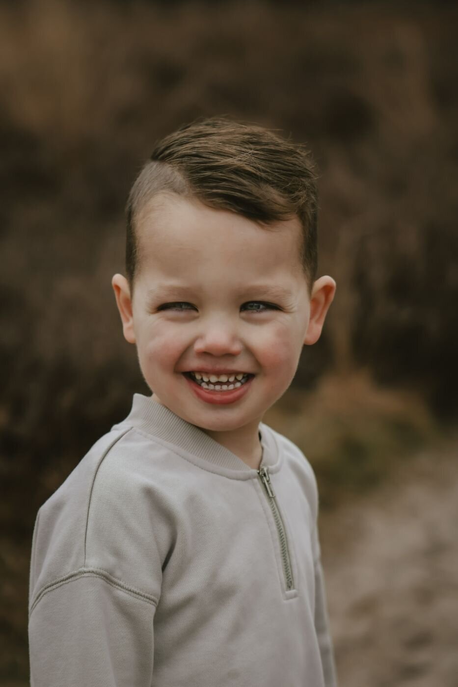Kinderfoto. Portret van een lachende jonge jongen met kort kapsel en een lichtgrijze sweater. Vrolijke jongen close-up.