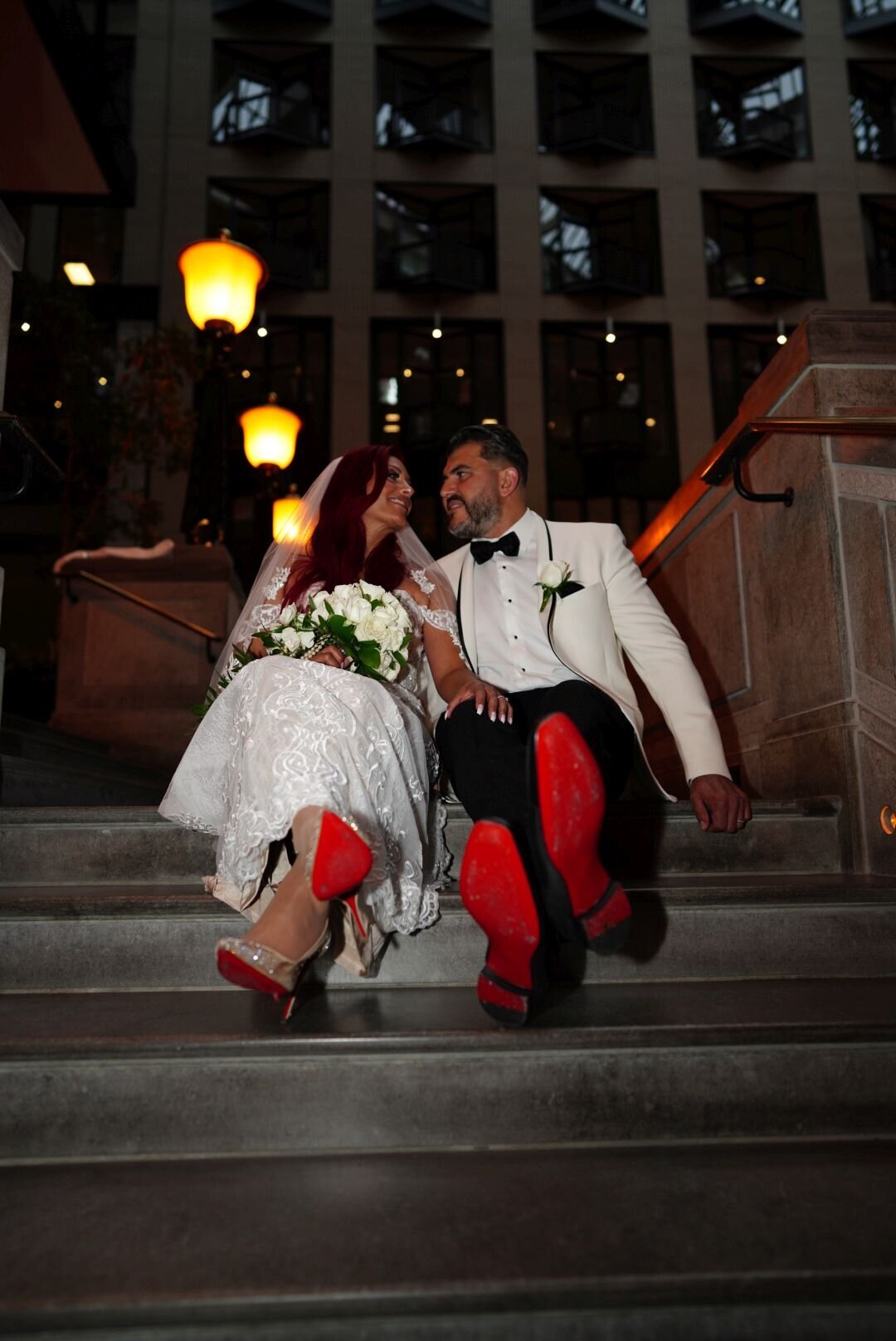 A couple sits on steps, proudly showing off their stylish shoes. Their relaxed and fun pose highlights their fashionable footwear and the easygoing nature of their relationship.