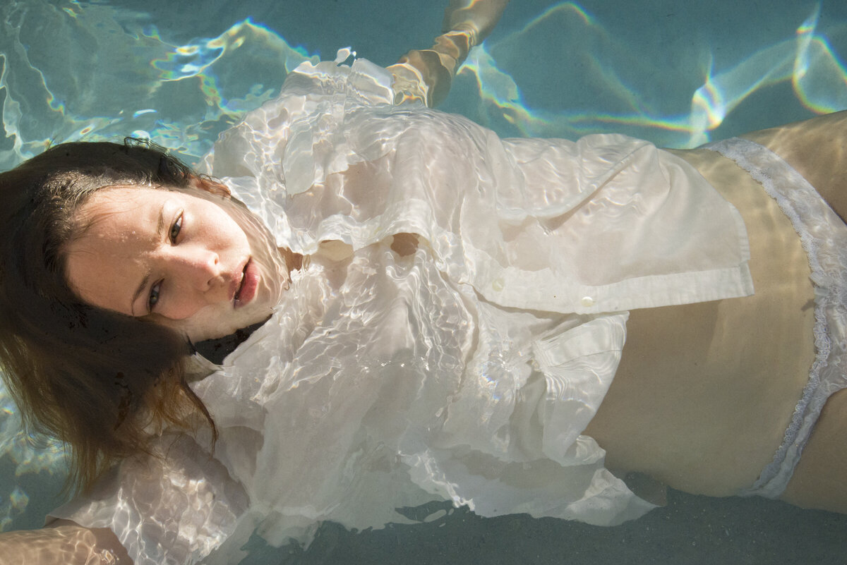 woman gazes at camera with disarming gaze as she floats in blue pool